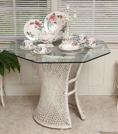Wicker table, 8-sided glass top, displaying a set of vintage china.