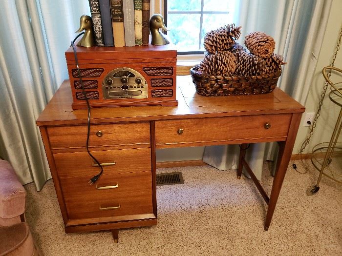 Sewing machine cabinet with machine; repop vintage radio; brass duck bookends; books, wicker basket and pine cones.