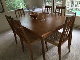 Teak dining table with pull out leaf each end w/ set of 6 woven seat chairs - From Scandinavian Design.