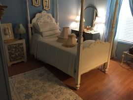 Four-poster twin bed, lamp shades, artwork, ladies dressing table in background