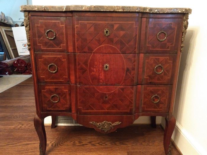 Early 20th century mahogany, fruitwood and marble commode in the Louis XV taste, having a shaped marble top above a conforming case with gilt mounts and three drawers, the drawers decorated with a floral marquetry cartouche surrounded by parquetry inlay panels, the whole rising on dainty cabriole legs ending in gilt sabots; measures 30.5" h x 27.5"w x 15"d.                                         Next picture is a better shot of the shaped marble top.