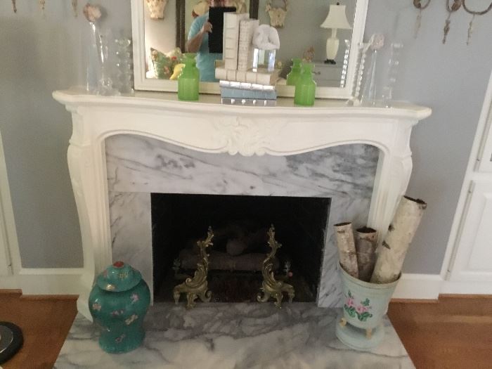 Brass andirons, lidded vase, wood pail, and white leather books on the mantle.