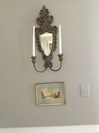 One of a pair of mirrored sconces and framed watercolors.