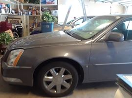 Champagne color sedan can be glimpsed in the background. Three car garage will be filled with art, supplies, kitchen items and small decorative accessories.