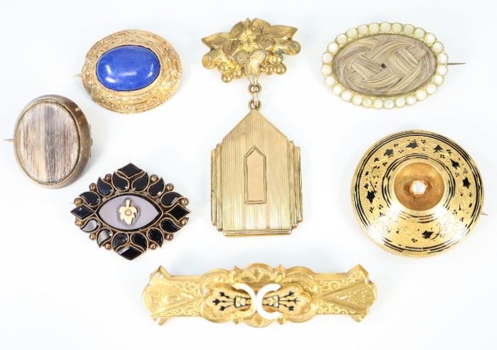 Seven 19th Century Brooches -  Including 2 Mourning brooches featuring encapsulated hair, 1 Jet Mourning brooch that is centered by a gold-tone leaf with seed pearl accent, 1 gold-plated brooch with suspended locket, 1 round and 1 rectangular gold-tone brooch with black enamel, and 1 gold brooch with oval lapis stone.  All are unmarked.  Wear to each, the black enamel is slightly worn and the setting of the lapis brooch is slightly misshapen.  Up to 2 1/2" long.  Totaling 56.4 grams.
