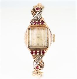 A Vintage Bulova Rose Gold, Diamond, & Ruby Ladies Wrist Watch -  14 kt Rose Gold watch with 6 diamond and 8 ruby enhancements about the face, on a double snake chain style bracelet.  Stamped "14KT".  Scratches noted, scuffs/nicks/flakes noted to the crystal.  Not running when cataloged.  Totaling 15.7 grams. 
