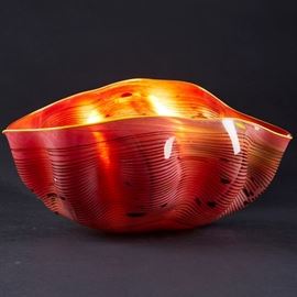Lot #47 Dale Chihuly (b. 1941). Red glass bowl with iridescent stripes from Chihuly's Macchia series. Signed and dated 1982 under the base. 
Provenance: Directly from artist
Collection of Edward Claycomb.
Biography: Dale Chihuly first encountered glass art as an interior design student at the University of Washington. Immediately fascinated, he went on to study glass at the University of Wisconsin, which was the first university in the United States to teach glassblowing. From there, he went on to the Rhode Island School of Design, where he continued to learn about glass and eventually ended up teaching. His education continued with a Fulbright Fellowship to go to the famous glassblowing studios of Venice. After his time in Italy, he returned to his home state of Washington to found his own glass school, the Pilchuck Glass School, with Ann and John Hauberg, influential supporters of the arts in Seattle. At this school, his art style and process truly flourished. In particular, Chihuly 