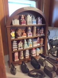 Ceramic spice containers in their own wooden shelf, behind antique metal irons.  