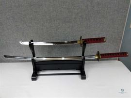 Set of Samurai Swords on Wooden Display / Handles are red ribboned. 17.5" Blade and 29" blade. Brass Hand guards. Both in Sheaths
