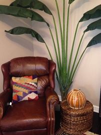 A comfortable leather chair, colorful pillow, large artificial plant, and baskets