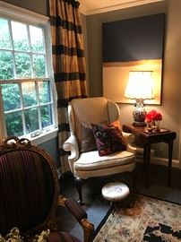 A white chair sitting by an antique pembrook table with  an antique blue and white porcelain lamp and a collection of small boxes including one cinnabar. The   Contemporary painting behind is an interesting work of textures pull together with a line  14 karat gold leaf 