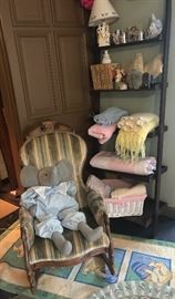 A collection of gifts for the newborn including hand knit throws silver cups and more in front of an antique Victorian rocker
