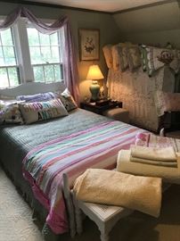 The girls bedroom, full-size white headboard sitting on a Stark light yellow bordered carpet.  A collection of spreads and pillow cases