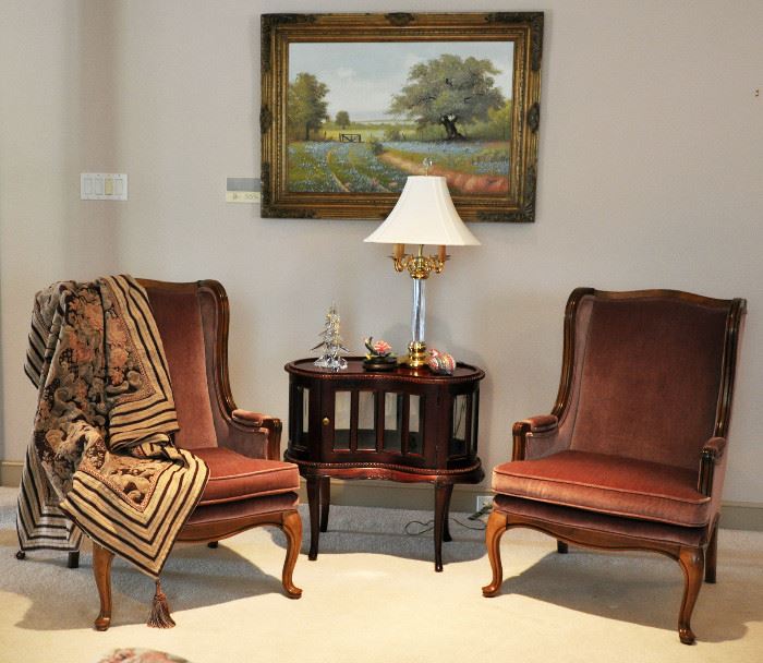 Pair of matching country French wing chairs flanking a very nice reproduction chocolate cabinet with a bluebonnet painting in the background