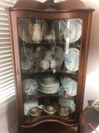 Antique porcelain and glass in an antique, quadruple bent glass door china cabinet