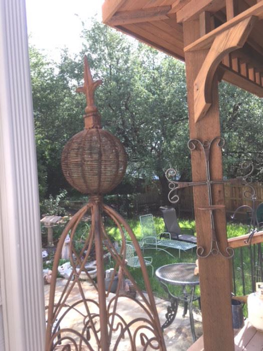 Numerous pieces of metal yard art, including hanging cross sconce and tall obelisk