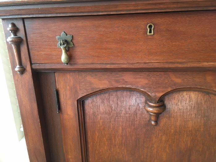 Detail of  carving and brass pulls and keyholes on oak sideboard with mirrored back splash.