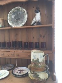 Detail of antique pine hutch. Various glazed transferware vessels from England. Set of red ruby stemmed glasses. Various collector plates in all sizes.