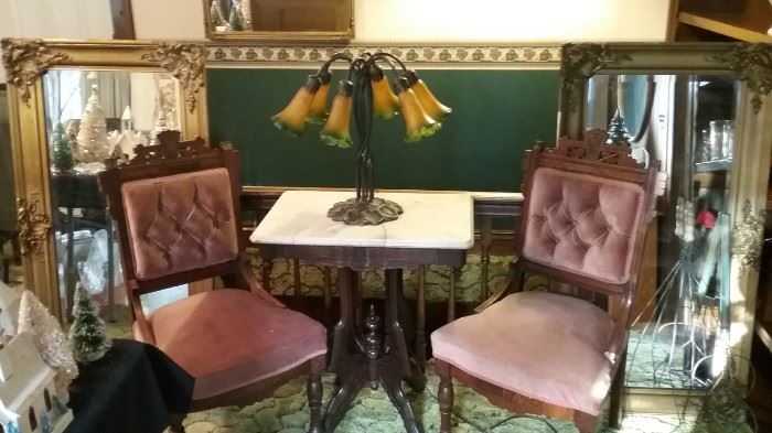 Two Eastlake chairs in front of beveled mirrors with golden frames.  