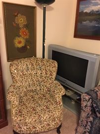 Working TV on stand. Needlepoint artwork, arm chair.