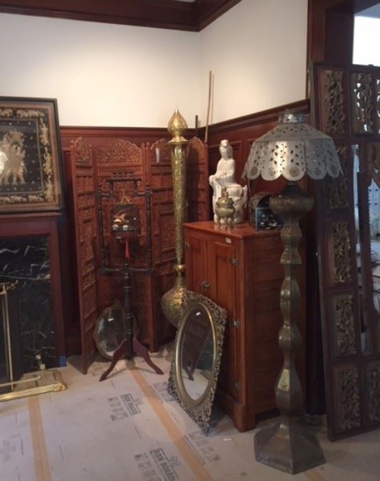 A view of the southeast corner of the dining room, showing a 4-panel carved wood floor screen, a bird cage hanging in a carved wood stand, a mirror framed in gilt wood, an antique ice box, and two tall, shapely Middle Eastern metalwork lamps. 