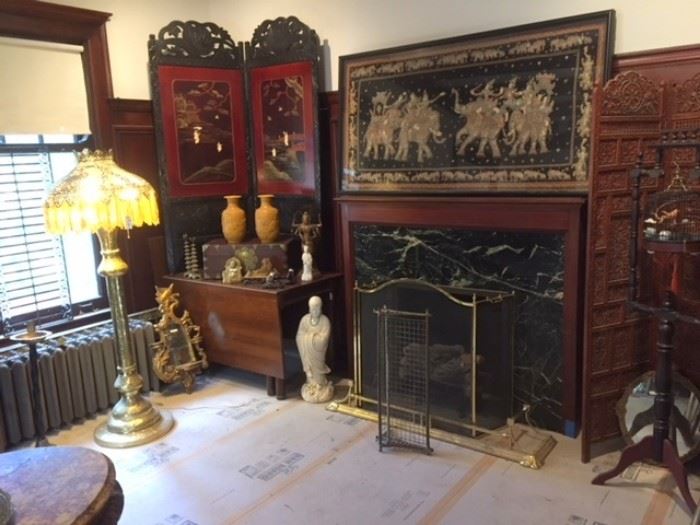 A view of the northeast corner of the dining room, showing a mid-century-modern Willet brand dining room table supporting an antique Japanese 2-panel wood & lacquer screen; two yellow Chinese ceramic vases inscribed on the bottom with the characters for "Wang Bing Rong," a famous Qing dynasty (1644-1911) ceramic artist; a large standing white Chinese porcelain figure; a tall standing Middle Eastern pierced & embossed brass lamp with unknown letters on the base and figural scenery in places; finally, a monumental, framed Burmese "kalaga" embroidery on the fireplace mantle. 