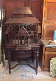 A Victorian bird cage with its original stand, in the dining room, next to an antique 2-piece wooden kitchen cabinet. 