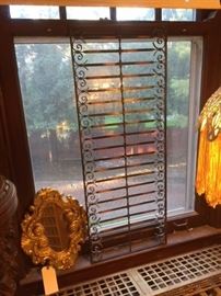Decorative metal grille in the dining room, next to a small gilt wood mirror. 
