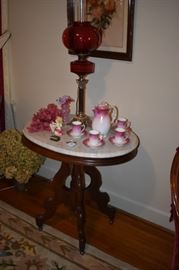 Antique Brass and Corinthian Columned Oil Lamp with Rare Dark Cranberry Glass Bowl and Shade. Beautiful Marble Topped Victorian Table is adorned with a Pink Fluted Edged Case Glass Vase an Antique Demitasse Set (Beautiful!)