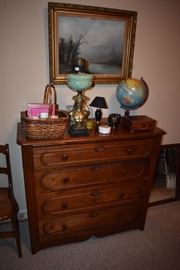 4 Drawer Antique Dresser with Beautifully Grained Wood Adorned with Beautiful Banquet Table Lamp Green (almost Slag like) Glass Bowl and Ornate Base also pictured is a Vintage World Globe, Woven Basket and other items