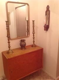 Foyer:  This mid-century cabinet has sliding doors.  On it are a pair of tall brass candlesticks and a vintage champleve vase made in Japan. The rectangular mirror is a brass color.  