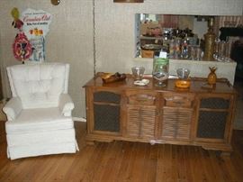 Family Room: A creamy white swivel/rocker chair by KROEHLER is next to a vintage tv/stereo cabinet.  The original TV has been replaced by a portable TV (priced separately) but the original RCA  turn table and radio are still intact.  On top of the cabinet are various vintage monkey-pod dishes, glassware, ash trays and a large container of matchbooks.