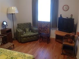Bedroom #2:  This room has a mix of vintage chairs, flip-top card table, vintage floor lamp, antique stool, newer TV cabinet and older TV, and a school desk.   