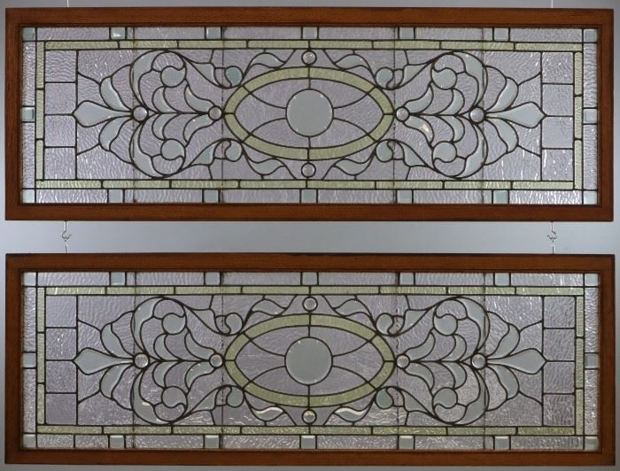 A Pair of late 19th century Stained Glass Transom Windows.  Multi color glass with clear bevels and cabochon glass accents in oak frames.  Some cracks to the panels, light wear overall.   Each 60 1/4"  x 21 1/4" high overall.  
