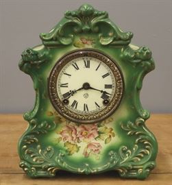 A turn of the century Ansonia "Wautauga" model china shelf clock.  8-day time and strike movement with a porcelain dial.  Green china case with floral decoration and gilded detail.  Some wear, overall crazing, hairlines in dial.  Running when cataloged.  12" high.
