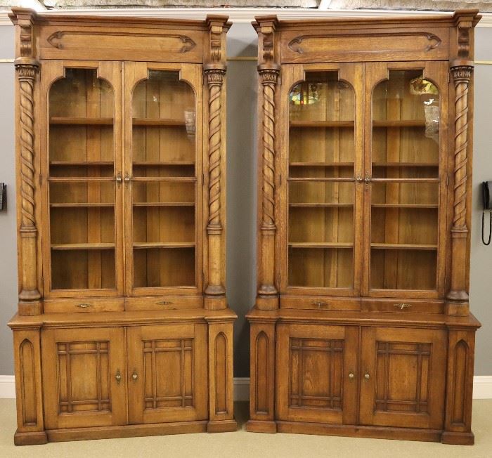 A pair of 19th century American Victorian Period Gothic Revival Butternut shop cabinets.  Two piece design with stepped, molded cornices above carved friezes and two glazed doors flanked by spiral turned column with carved capitals and two lower drawers on bases with two paneled doors flanked by Gothic pilasters on stepped molded bases.  Older refinishing with minor wear, replaced upper shelves and Brass hardware.  Each 58 1/2 x 24 1/2 x 108" high overall. 
