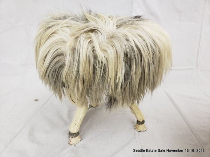 Long-haired round footstool with tri-footed animal-form legs and hoofed feet.