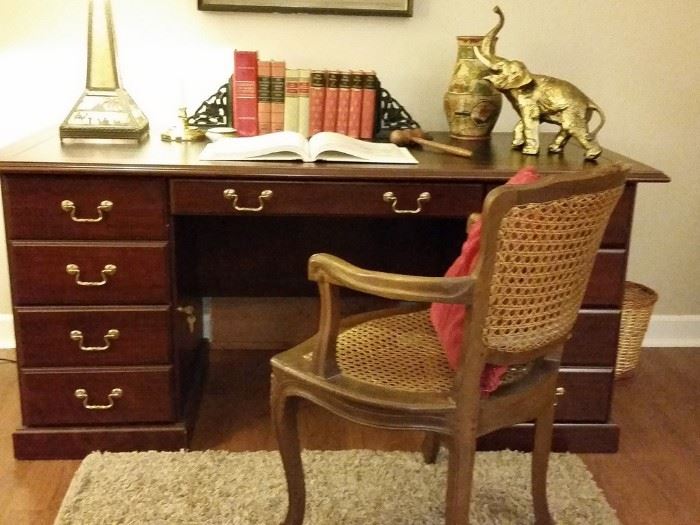 Office desk. Vintage collectible books and brass elephant.  Mid-century cane back french provincial style chair. 