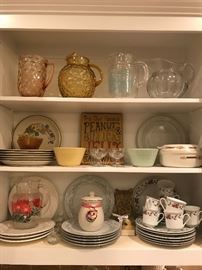 one of the many cabinets in the kitchen filled with vintage and contemporary items including water and juice pitchers and old glass and crock bowls