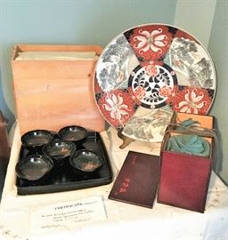 This amazing Imari plate measures 18" in circumference. The bowls are a set of 10 and come with a certificate of authenticity. The set of 5 black lacquer trays are in their original rice paper wrappings inside the wooden box.  The box on the right is for the antique bowls.