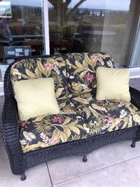Outdoor wicker love seat with cushions and sold with matching chair and ottoman 