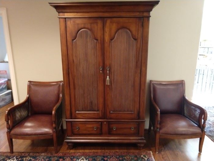 Stately wooden armoire, flanked by a pair of leather/cane armchairs, by "Our House Designs".