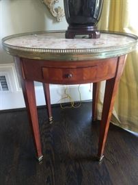 Close-up of the French bouillotte table, with inlaid wood, pink marble top, brass gallery, single drawer and candle slides.