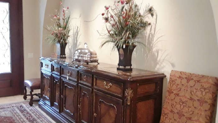 this extra long buffet used as a striking entry piece is by Marg Carson. Vintage venison server with dome and tray stand that can be heated with hot water. Pair of dry flower arrangements. Two of the ten dining chairs.