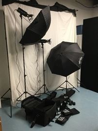 Britek Photography Studio Light and Background Set. Includes 3 HS-1000 professional studio lights with light stands, 2 umbrellas, 2 softboxes, sync cords, power cords, several attachments (barndoor, snoot, and more), background stand, and muslin backdrops.  All equipment comes in original cases. 