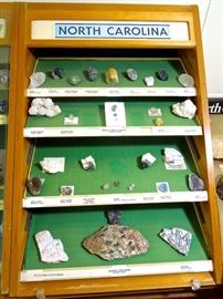 Lot 118: North Carolina Rough Gems and Minerals in Display Case
Second small case of NC gems and minerals in wood case with removable sliding glass front. Case is 20" W x 30" H x 25" D. Features a group of Emerald in Matrix and faceted Aquamarine. For complete list of rocks in this group see photos. When bidding on this case and contents, please keep in mind that you will be responsible for removing it from the residence. It is located in the basement and will have to be taken up a narrow flight of stairs. Please bring your own packing and moving material as well as muscle. Will schedule a specific time to avoid overcrowding during pickup.