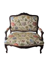 Antique French carved settee beautifully upholstered in a hand woven silk floral vine motif. Fabric features a vibrant royal blue, cornflower blue, lilac, dark and light hues of rose with forest green and lighter green leaves on an ecru background. Double self welt grim throughout (including arms). Intricate carved detail on the crest and center apron resembling a pineapple symbol and acanthus leaf detail throughout including on cabriole legs. The back of the sofa has an exposed wood frame with a center splat which makes it eye-catching floated in a room as well as against a wall. The frame has been refurbished in a rich walnut stain and newly upholstered in a stunning floral fabric.                                                 Dimensions: 41”w x 23”d x 40.5”h • Seat=24”d x 17”h • Arm=24”h
