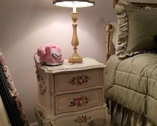 Painted floral two drawer nightstand with push button pink phone and table lamp, also bolts of upholstery fabric