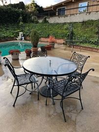 Patio set: round, glass-top table and four wrought-iron chairs with Sunbrella-brand umbrella