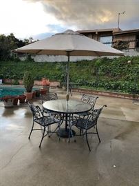 Patio set: round, glass-top table and four wrought-iron chairs with Sunbrella-brand umbrella
